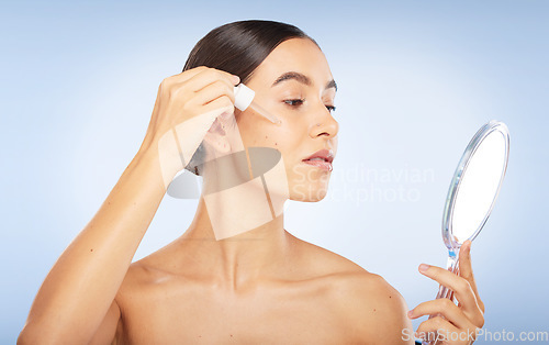 Image of Face, skincare serum and woman with mirror in studio on a blue background. Beauty, cosmetics and female model with hyaluronic acid, essential oil and dropper product for healthy skin or anti aging.