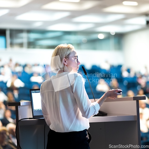 Image of Female speaker giving a talk on corporate business conference. Unrecognizable people in audience at conference hall. Business and Entrepreneurship event.