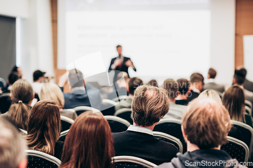 Image of Speaker giving a talk in conference hall at business event. Rear view of unrecognizable people in audience at the conference hall. Business and entrepreneurship concept.