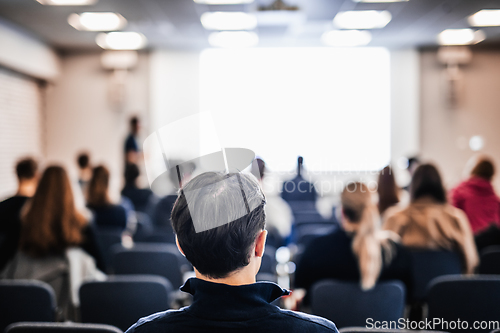 Image of Speaker giving a talk in conference hall at business event. Rear view of unrecognizable people in audience at the conference hall. Business and entrepreneurship concept.