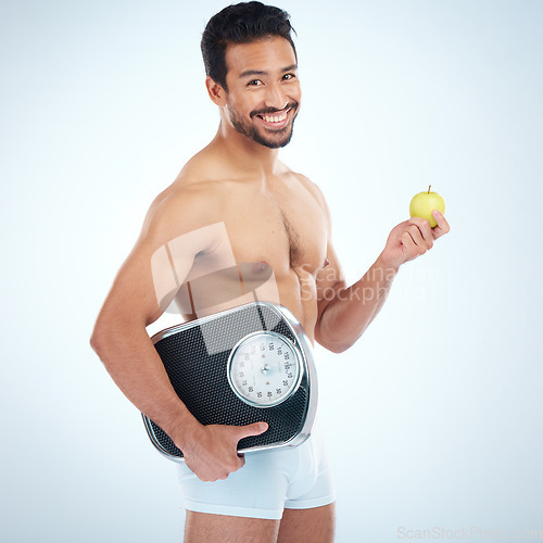 Image of Portrait, fitness and man with apple and scale in studio isolated on a blue mockup background. Weight loss, healthy diet and happy male model with fruit or food for nutrition, vitamin c and wellness.