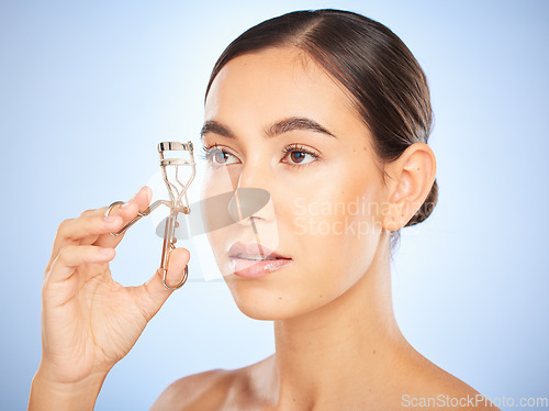 Image of Beauty, makeup and woman with an eyelash curler in a studio for a trendy cosmetic face routine. Cosmetics, clean and girl model from Canada doing natural make up with a lash curl by a blue background