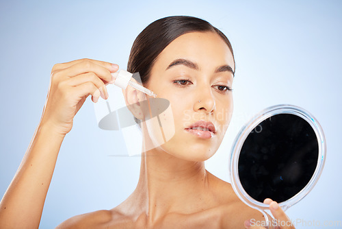 Image of Face, skincare serum and woman with mirror in studio on a blue background. Beauty, cosmetics and female model with hyaluronic acid, essential oil and dropper product for healthy skin or anti aging.