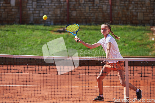 Image of A young girl showing professional tennis skills in a competitive match on a sunny day, surrounded by the modern aesthetics of a tennis court.