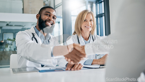 Image of Handshake, partnership or happy doctors in a meeting after successful medical surgery or reaching healthcare goals. Teamwork, woman or black man smiles shaking hands with a worker in hospital office