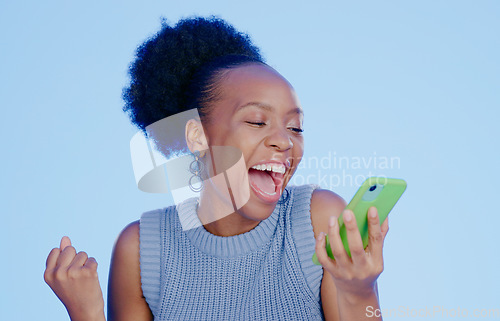 Image of Celebration. phone and young black woman in a studio with winning, achievement or success. Happy, smile and African female winner cheering with fist pump on cellphone isolated by blue background.