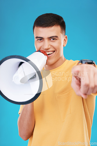 Image of Megaphone, happy and portrait of man in studio pointing for announcement, speech or rally. Smile, protest and young person from Canada with bullhorn for loud communication isolated by blue background