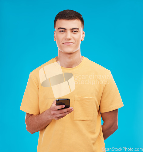 Image of Phone, portrait and young man in studio networking on social media, mobile app or internet. Smile, technology and male person from Canada scroll on website with cellphone isolated by blue background.