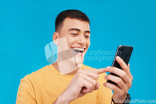 Image of Phone, excited and young man in a studio scroll on social media, mobile app or the internet. Smile, happy and male person from Canada networking on website with cellphone isolated by blue background.