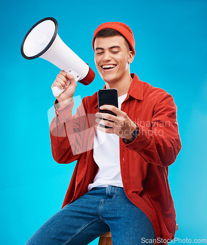 Image of Phone, megaphone and young man in a studio reading announcement or speech for a rally. Happy, cellphone and male activist or protest with bullhorn for loud communication isolated by blue background