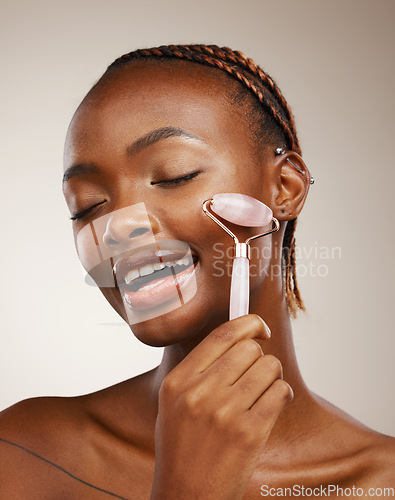 Image of Woman, face roller and massage in studio for skincare, rose quartz cosmetics and aesthetic dermatology on brown background. African model, crystal stone tools and lymphatic drainage for facial beauty