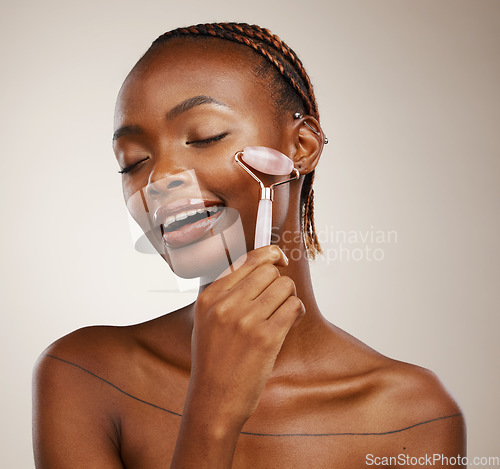 Image of Happy woman, face roller and massage for beauty, rose quartz cosmetics and aesthetic dermatology in studio on brown background. African model, crystal stone and lymphatic drainage for facial skincare