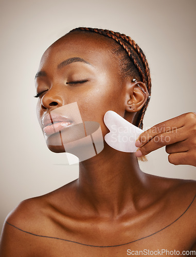 Image of Woman, beauty and gua sha for face massage, aesthetic skincare and anti aging dermatology in studio on grey background. African model, crystal stone tools or lymphatic drainage with facial cosmetics