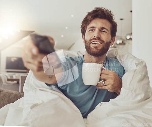 Image of Coffee, relax and a man in a blanket watching tv on a sofa in the living room of his home for entertainment streaming. Movie, television or subscription with a happy young person using a remote