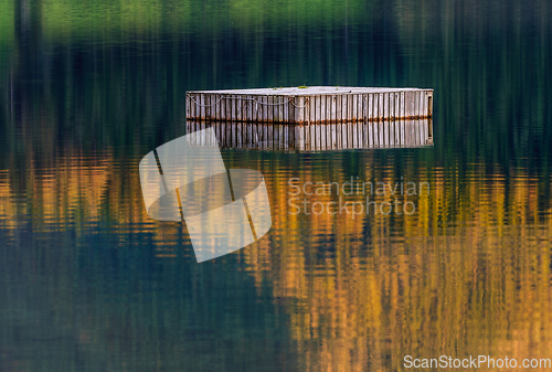 Image of old wooden raft reflecting in water with autumn colours