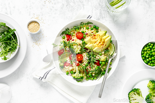 Image of Couscous salad with broccoli, green peas, tomatoes, avocado and fresh arugula. Healthy natural plant based vegetarian food for lunch, israeli cuisine, top view