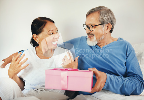 Image of Senior, man and woman with gift in bedroom for anniversary, romantic or together. Asian, elderly couple and bond by smile in happiness for celebration by surprise expression on face, embrace and love