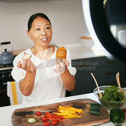 Image of Asian woman, vegetables and live streaming for cooking with bottle, healthy food and blog on social media in kitchen. Chef, mature influencer and content creation, class and broadcast online tutorial