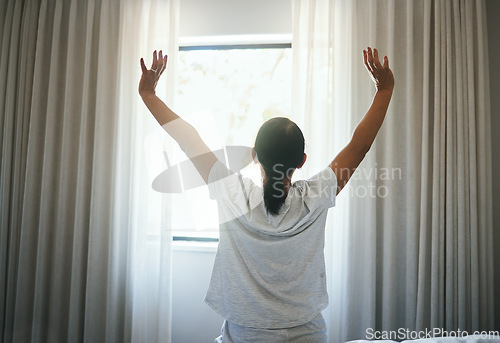Image of Stretching, curtains and back of woman at window for wake up, sunrise or good morning routine in bedroom at home. Awake, arms or get up from comfortable sleep to start bright new sunny day after rest