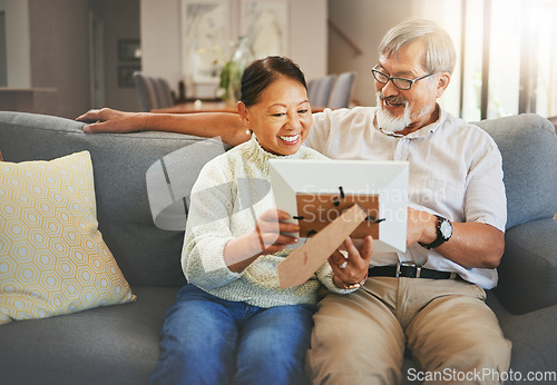 Image of Elderly couple, happy and together with memory or photograph on sofa with smile in living room. Senior man, woman and married with embrace by sit, bond and love in relationship for vacation, holiday