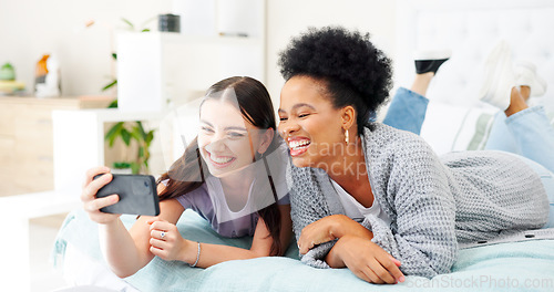 Image of Happy, selfie and girl friends on a bed for bonding and relaxing together with a phone. Smile, technology and interracial female people taking a picture with cellphone in bedroom of modern apartment.