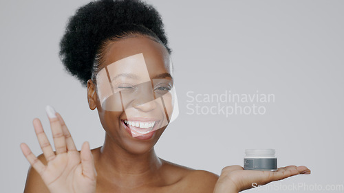 Image of Woman, model and hand with cream for face, cosmetic and beauty aesthetic with wink for happiness. Black person, portrait and dermatology with smile for product, mockup and grey studio background