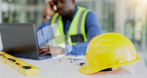 Image of Engineering, construction tools and architect with helmet on desk with break from project, worksite or renovation. African, person or foreman with laptop to review of plans, building or real estate