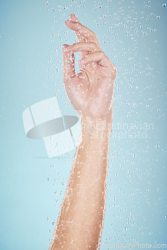 Image of Water drops, hand and closeup with cleaning, shower and morning dermatology in studio. Blue background, person arm and splash for wellness, washing and skin glow with self care and hygiene safety