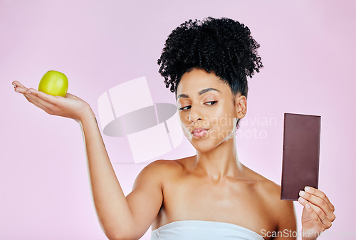 Image of Woman in studio with apple, chocolate and decision for food, wellness and skincare nutrition. Fruit vs sugar, diet and choice for beauty model on pink background with challenge for healthy eating.