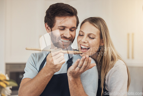 Image of Couple, cooking and taste test in kitchen with romance, support and love in their home together. Food, spoon and man feeding woman in house while preparing a delicious meal with fun and bonding