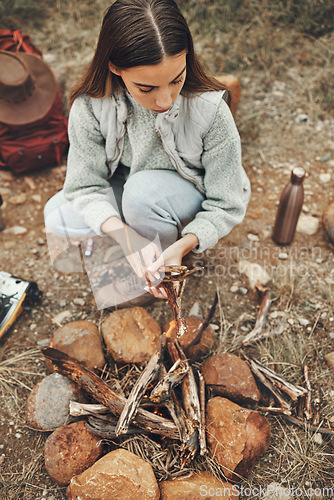 Image of Wood, nature and woman with fire on a camp on a mountain for adventure, weekend trip or vacation. Stone, sticks and young female person making a flame or spark in outdoor woods or forest for holiday.