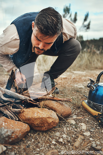 Image of Wood, nature and man with fire on a camp on a mountain for adventure, weekend trip or vacation. Stone, sticks and young male person making a flame or spark in outdoor woods or forest for holiday.