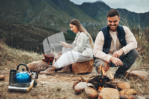 Image of Wood, nature and couple with fire on a camp on a mountain for adventure, weekend trip or vacation. Stone, sticks and young man and woman making a flame or spark in outdoor woods or forest for holiday