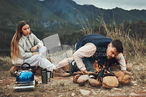 Image of Wood, mountain and couple with fire on a camp in nature for adventure, weekend trip or vacation. Stone, sticks and young man and woman making a flame or spark in outdoor woods or forest for holiday.