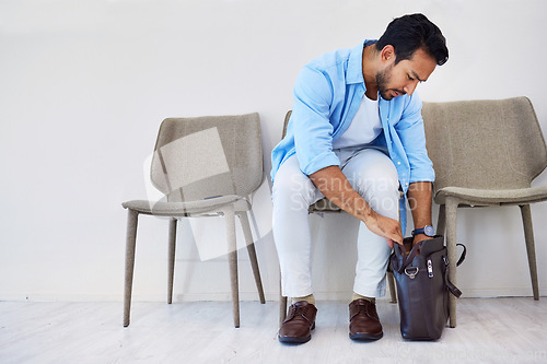 Image of Man, interview and job in waiting room, chair and looking for cv in bag by wall background. Business person, recruitment and marketing opportunity or vacancy, human resources and hiring for position