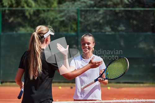 Image of Two female tennis players shaking hands with smiles on a sunny day, exuding sportsmanship and friendship after a competitive match.