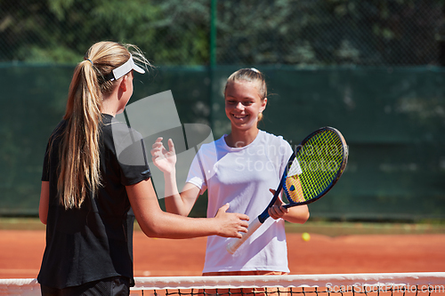 Image of Two female tennis players shaking hands with smiles on a sunny day, exuding sportsmanship and friendship after a competitive match.