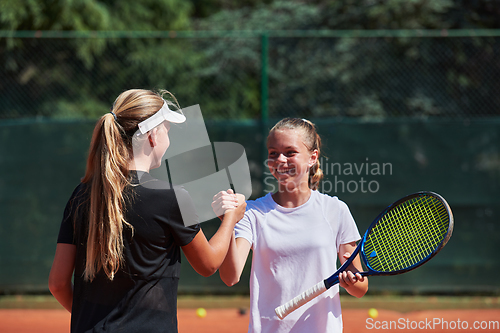 Image of Two female tennis players shaking hands with smiles on a sunny day, exuding sportsmanship and friendship after a competitive match.