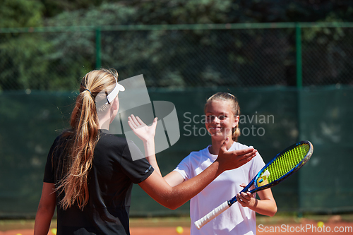 Image of Two female tennis players shaking hands with smiles on a sunny day, exuding sportsmanship and friendship after a competitive match.