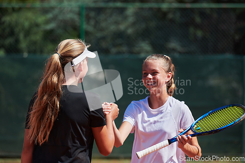 Image of Two female tennis players shaking hands with smiles on a sunny day, exuding sportsmanship and friendship after a competitive match.