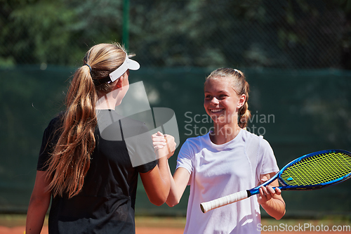 Image of Two female tennis players shaking hands with smiles on a sunny day, exuding sportsmanship and friendship after a competitive match.