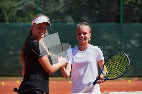 Image of Two female tennis players shaking hands with smiles on a sunny day, exuding sportsmanship and friendship after a competitive match.