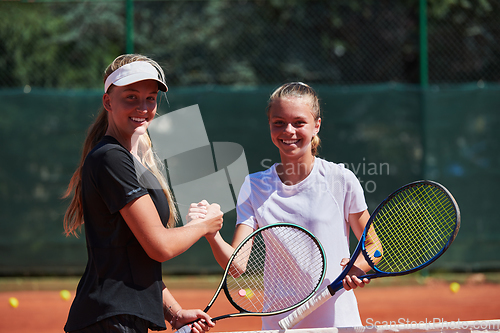 Image of Two female tennis players shaking hands with smiles on a sunny day, exuding sportsmanship and friendship after a competitive match.