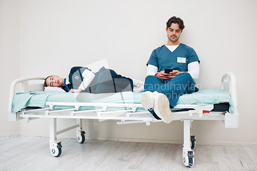 Image of Tired doctors, woman and man in hallway with phone, texting and relax on bed at hospital job. Medic team, partnership or friends with burnout, smartphone and fatigue with healthcare, clinic and rest