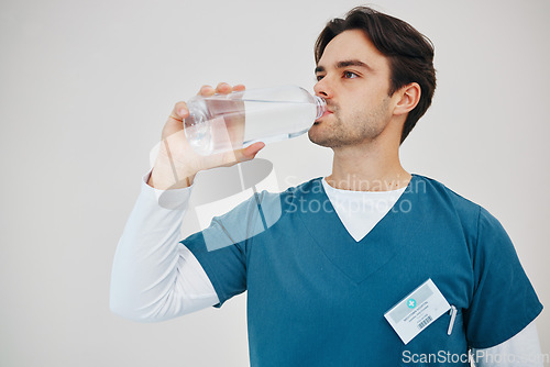 Image of Surgeon, man drinking water in bottle and health, wellness or body nutrition in studio isolated on white background in hospital. Medical professional, hydration and liquid of thirsty nurse on break