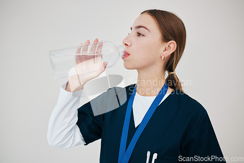 Image of Nurse, woman drinking water in bottle and health, wellness or body nutrition in studio isolated on white background in hospital. Medical professional, hydration and liquid of thirsty surgeon on break