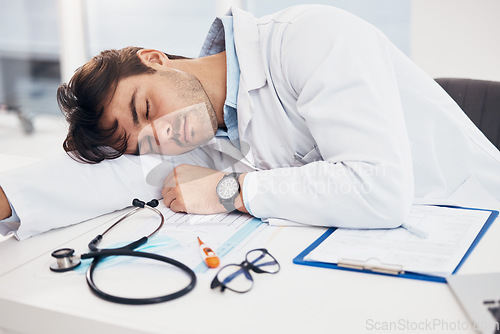 Image of Healthcare, tired and a doctor man sleeping at his desk in the hospital with fatigue or exhaustion. Medical, burnout and an overworked young medicine professional asleep in his office at the clinic