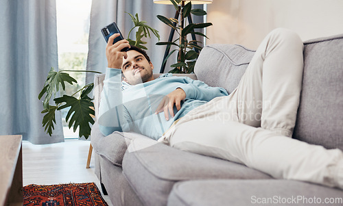 Image of Man, phone and relax on sofa for social media, communication or entertainment in living room at home. Male person lying on lounge couch with mobile smartphone for online app or streaming at house