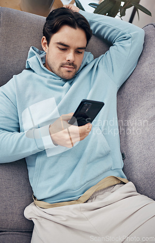 Image of Man, phone and relax on sofa for social media, communication or networking in living room at home. Male person lying on lounge couch for online chatting or texting on mobile smartphone app at house