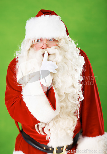 Image of Santa claus, finger and quiet secret in studio for Christmas surprise, celebration or holiday excitement. Male person, hand gesture and hush emoji for winter vacation joy, green background or mockup